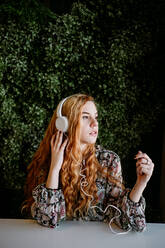 Pretty young redhead woman putting on headphones at the bush. - ADSF02701