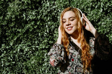 Pretty young redhead woman putting on headphones at the bush. - ADSF02703