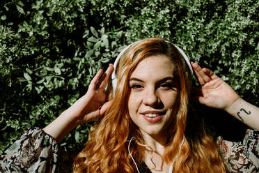 Pretty young redhead woman putting on headphones at the bush. - ADSF02704