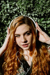 Pretty young redhead woman putting on headphones at the bush. - ADSF02705