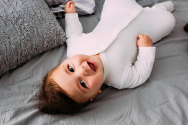 From above shot of cute baby lying on soft bed and laughing. - ADSF02719
