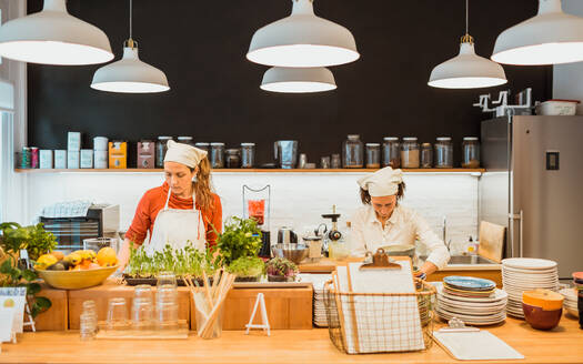 Zwei hübsche Frauen arbeiten zusammen und kochen in der Küche eines Cafés. - ADSF02747