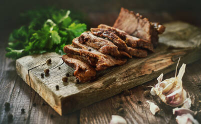 Frischer Knoblauch und Petersilie liegen auf dem Holztisch neben der Tafel mit leckeren gebackenen Schinkenscheiben - ADSF02768