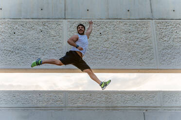 Attraktiver bärtiger Mann in Sportkleidung lächelt und springt hoch beim Training im Freien auf der Straße - ADSF02873