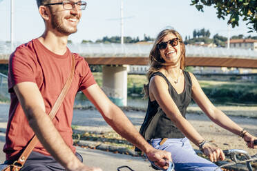 Cheerful couple riding bicycles in park during sunny day on weekend - SBAF00022