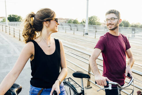 Paar im Gespräch, während es mit Fahrrädern auf einer Brücke gegen den klaren Himmel läuft - SBAF00025