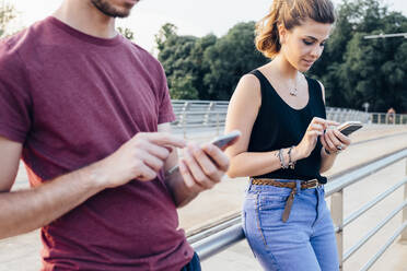 Couple using smart phones while standing on bridge - SBAF00027