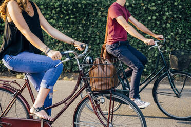 Couple riding bicycles on road against plants in park - SBAF00028