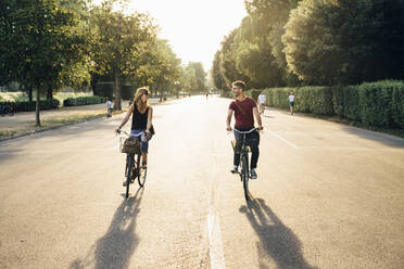 Happy couple cycling on road amidst trees in park during sunset - SBAF00029