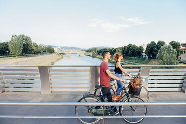 Paar mit Fahrrädern zu Fuß auf Brücke über Fluss gegen Himmel - SBAF00034