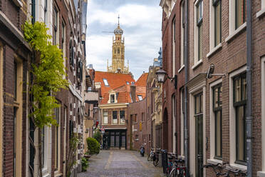 Niederlande, Nordholland, Haarlem, Leere Gasse zwischen alten historischen Häusern mit Turm der Bakenesserkerk im Hintergrund - TAMF02541