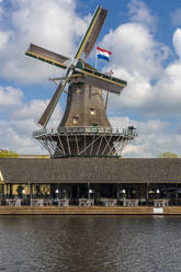 Niederlande, Südholland, Leiden, Restaurant am Flussufer vor der historischen Windmühle DHeesterboom im Hintergrund - TAMF02556