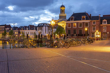 Niederlande, Südholland, Leiden, Fahrräder entlang der beleuchteten Altstadtstraße in der Abenddämmerung geparkt - TAMF02611