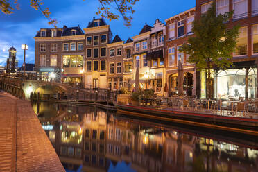 Netherlands, South Holland, Leiden, Sidewalk cafe and row of townhouses reflecting in Nieuwe Rijn canal at dusk - TAMF02613