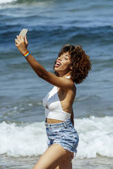 Young woman with eyes closed taking selfie while standing in sea on sunny day - OCMF01477