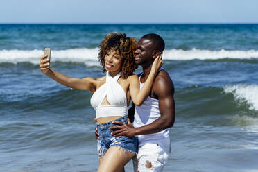 Junge Frau, die ein Selfie mit ihrem Freund macht, während sie im Meer steht - OCMF01484