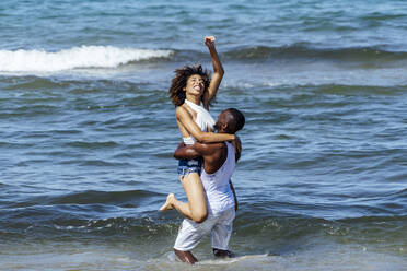 Romantic young man carrying girlfriend while standing in sea - OCMF01488
