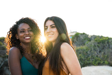 Schöne verschiedene junge Frauen stehen eng und lächelnd glücklich auf dem Hintergrund der Natur im Hintergrund beleuchtet - ADSF02907