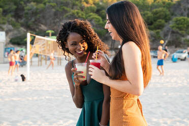 Playful women enjoying drinks on beach - ADSF02911
