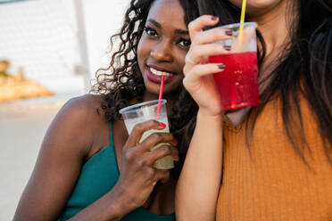 Playful women enjoying drinks on beach - ADSF02914