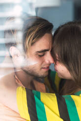 Side view of handsome young man and lovely woman kissing passionately while standing near window at home - ADSF02919