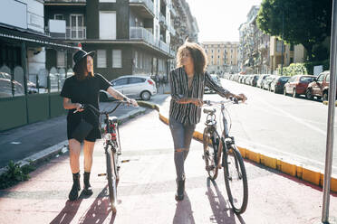 Couple talking while walking with bicycles on street in city - MEUF01546