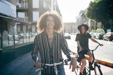 Smiling couple riding bicycles on city street during sunny day - MEUF01548