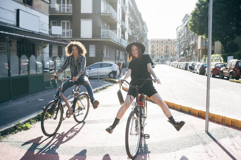 Glückliches Paar auf Fahrrädern auf einer Straße in der Stadt an einem sonnigen Tag - MEUF01550