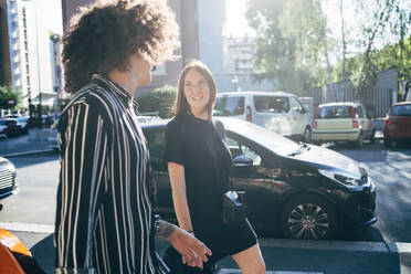 Paar im Gespräch beim Spaziergang auf der Straße in der Stadt an einem sonnigen Tag - MEUF01565