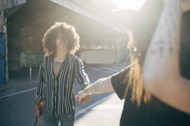Lächelnder Mann, der die Hand seiner Freundin hält, während er an einem sonnigen Tag auf einer Straße in der Stadt steht - MEUF01569