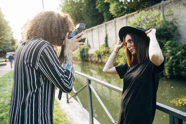 Man photographing girlfriend with camera while standing in park - MEUF01578