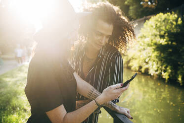 Paar, das ein Smartphone benutzt, während es an einem sonnigen Tag im Park steht - MEUF01580