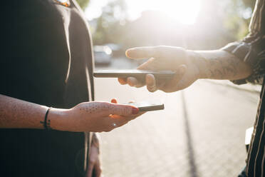 Close-up of couple scanning code through smart phones in city during sunny day - MEUF01590