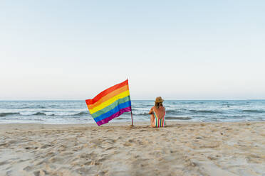 Marure woman sitting on the beach with gay pride flag - CJMF00315