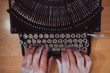 Von oben aufgenommene Hände einer anonymen älteren Person, die auf der Tastatur einer alten Schreibmaschine tippt - ADSF02964