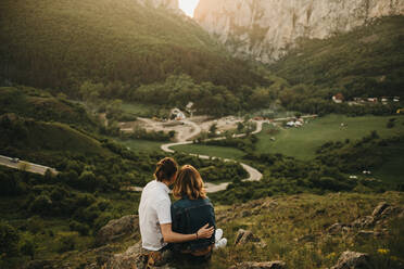 Cute couple hugging and toughing foreheads while sitting on rocky slope on background of beautiful valley and mountains - ADSF02978