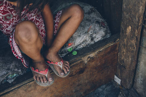 Crop shot from above of poor little girl sitting on weathered mattress in bad condition on wooden bed - ADSF02984