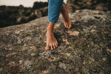 Crop barefoot woman in jeans walking on rock - ADSF02997