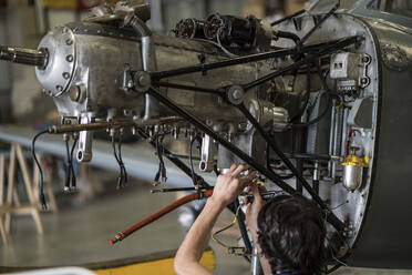 Die Hände eines Flugzeugmechanikers, der den Motor eines kleinen Flugzeugs im Hangar repariert - ADSF03106