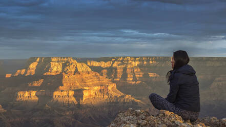 USA, Arizona, Rückansicht einer auf einem Felsen sitzenden Frau am Grand Canyon bei Sonnenuntergang - TOVF00211