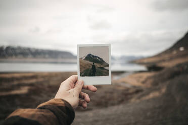 Crop hand holding instant shot with tourist and hill at the lake in Iceland. - ADSF03143