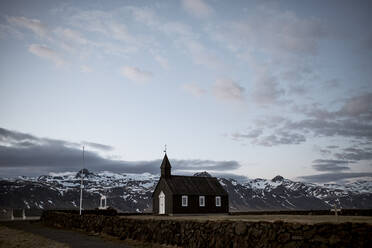 Kleines schwarzes Kirchengebäude auf dem Feld in den verschneiten Bergen in Island - ADSF03146