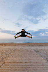 Handsome man in sportswear jumping high during outdoor training on sandy beach - ADSF03203