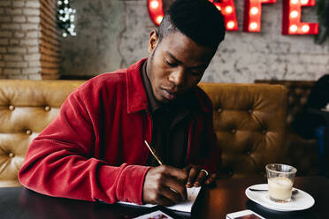 Seriöser afrikanischer Mann in roter Jacke Brief am Tisch im Café - ADSF03214