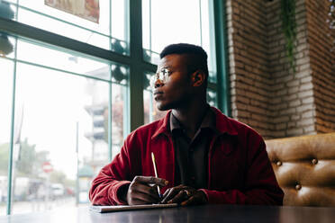 Seriöser afrikanischer Mann in roter Jacke Brief am Tisch im Café - ADSF03215