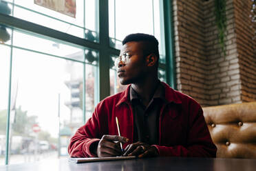 Serious african male in red jacket letter at table in cafe - ADSF03215