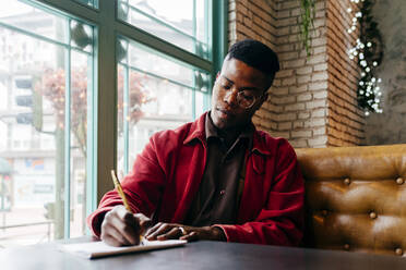 Serious african male in red jacket letter at table in cafe - ADSF03216