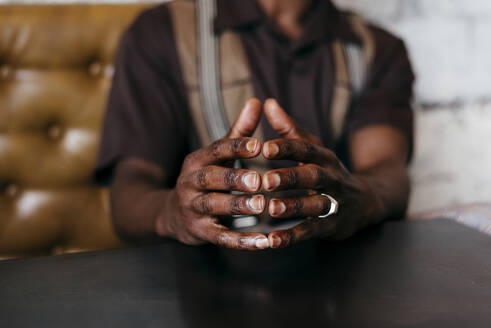 Ausschnittansicht der gefalteten Hände eines sitzenden gesichtslosen afrikanischen Mannes in Hosen - ADSF03223