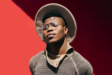 Junger Afrikaner im Pullover, weißer Hut und Brille auf rotem Hintergrund - ADSF03229