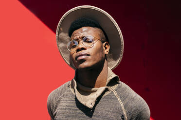 Young african male in sweater white hat and glasses on red background - ADSF03229